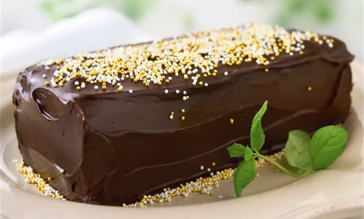 Chokladlängd med blank mörk tryffelglasyr, dekorerad med gulvita strössel, serverad på crèmefärgad tallrik med grön myntakvist