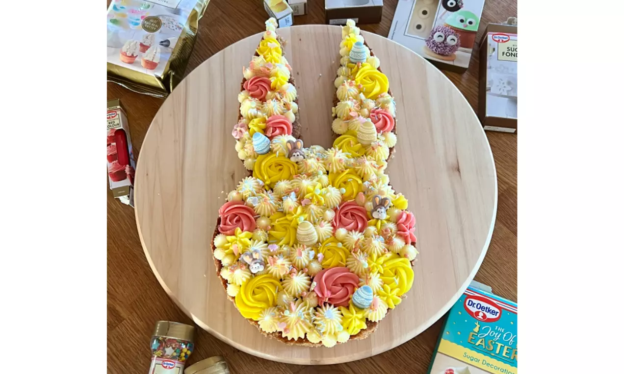 Morotskaka formad som en vit kanin med rosor och toppad med gula, vita och rosa gräddkrämsblommor på en rund träbricka